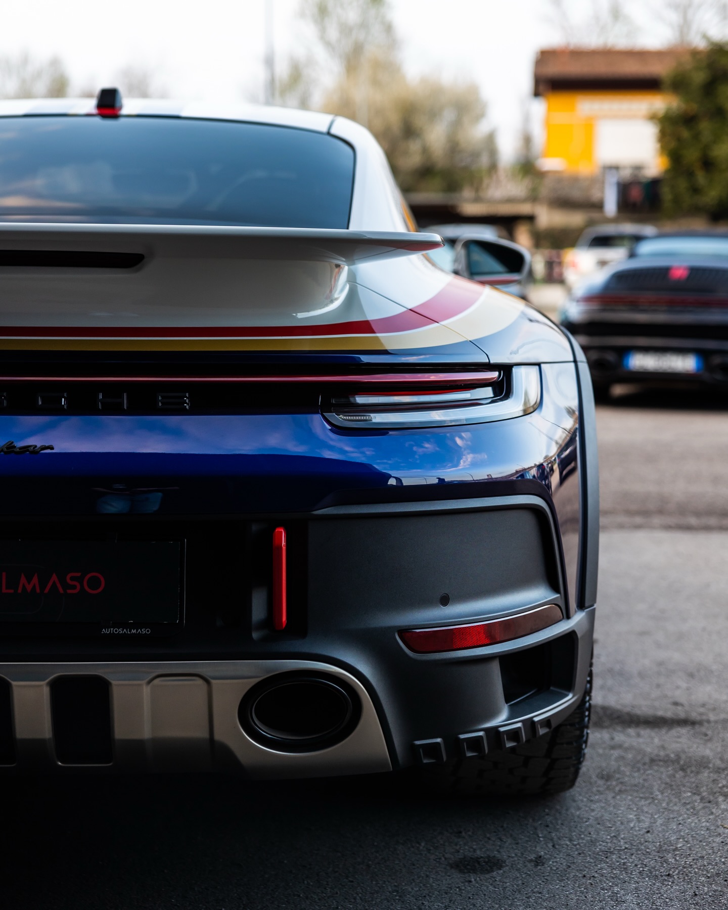 Retro di Porsche blu e bianca con strisce rosse e oro e portatarga AutoSalmaso, altre auto nel piazzale